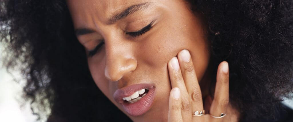 Woman having TMJ pain holding cheek.